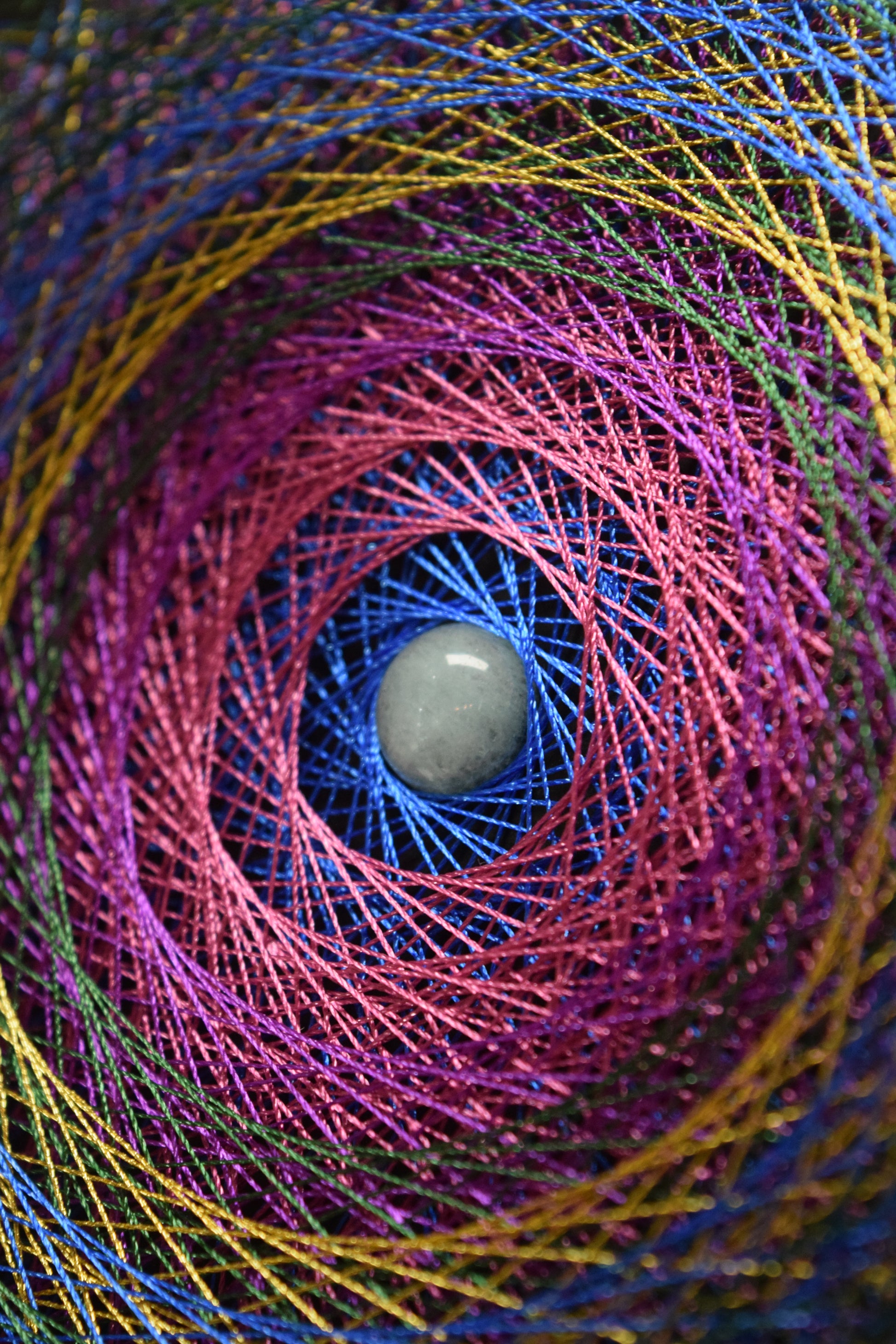 Focus pe cristal rotund Angelit in centrul mandalei din cuie si ata stralucitoare, in culori vii.