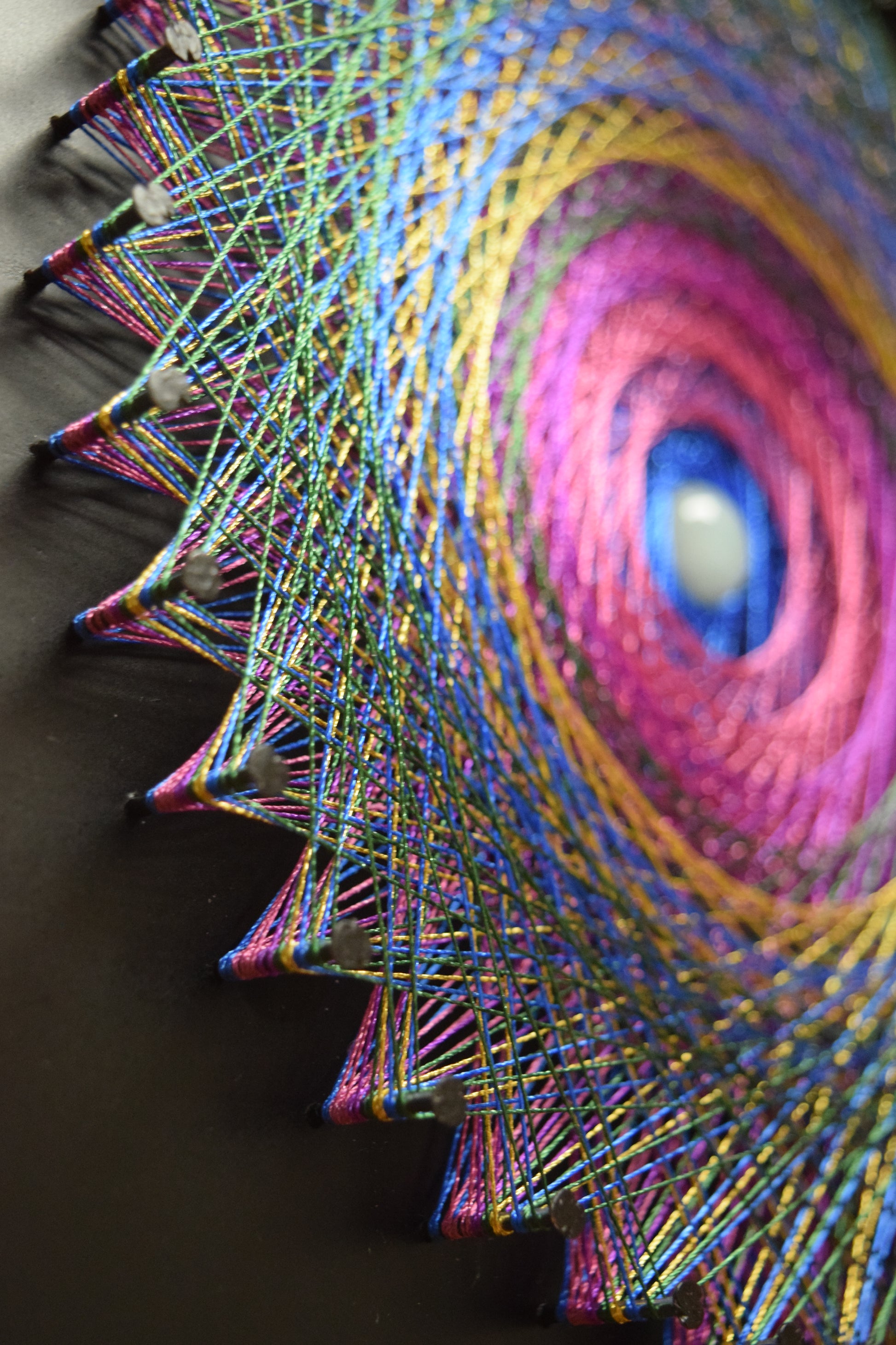 Mandala creata din cuie si ata, o mandala in culori vii, ata straluceste in lumina.