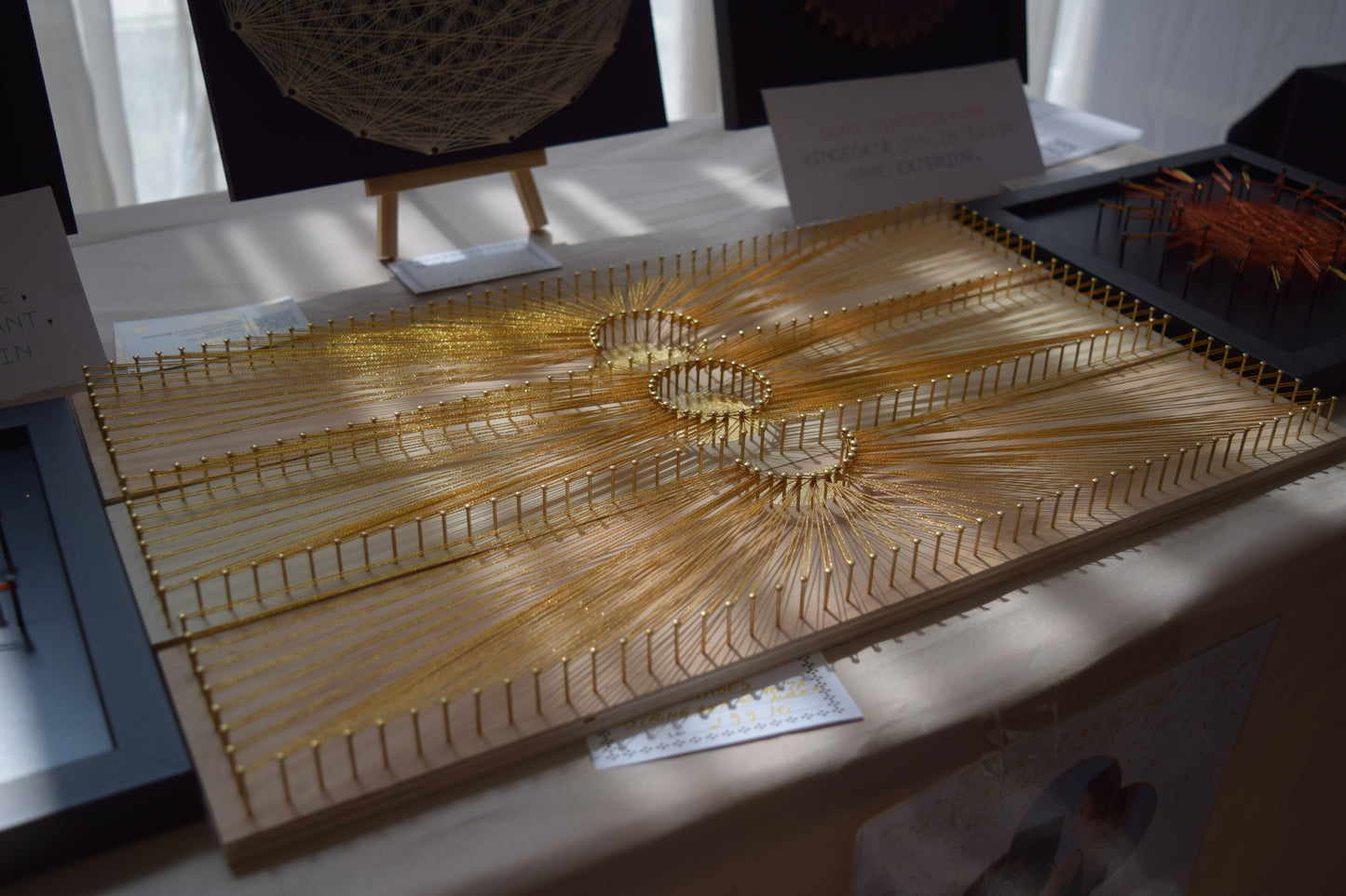 Sun Phases artwork set on table, illuminated by sunlight – gold leaf and shiny thread sparkling on natural wood base.