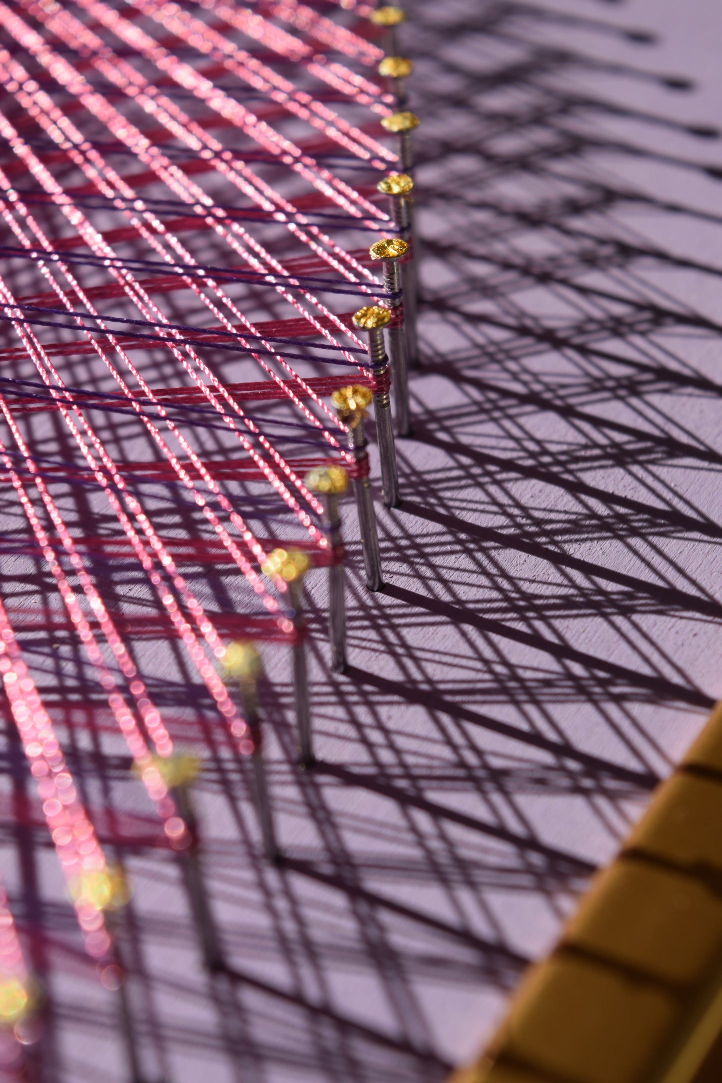 Detail of Yin Yang string art with visible nail texture and artistic shadow play from violet and pink threads.